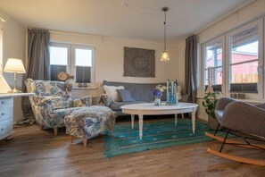 Ein Wohnzimmer mit Sofa, Sesseln, Hocker, Couchtisch und einer Pendelleuchte.