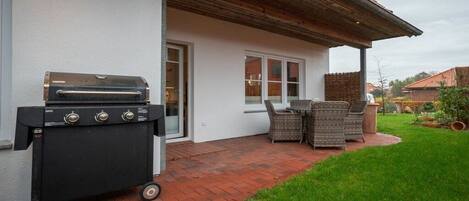 A patio with a grill, wicker furniture, and a brick pathway leading to a house.