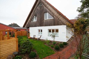 Ein zweigeschossiges Haus mit geneigtem Dach, einem kleinen Vorgarten mit einer Holzterrasse und einem gepflasterten Weg.
