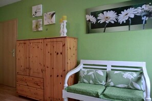 A room with a wooden wardrobe, a white bench with green cushions, and floral wall art. - Holiday home in Graal-Müritz with terrace (Graal-Müritz)