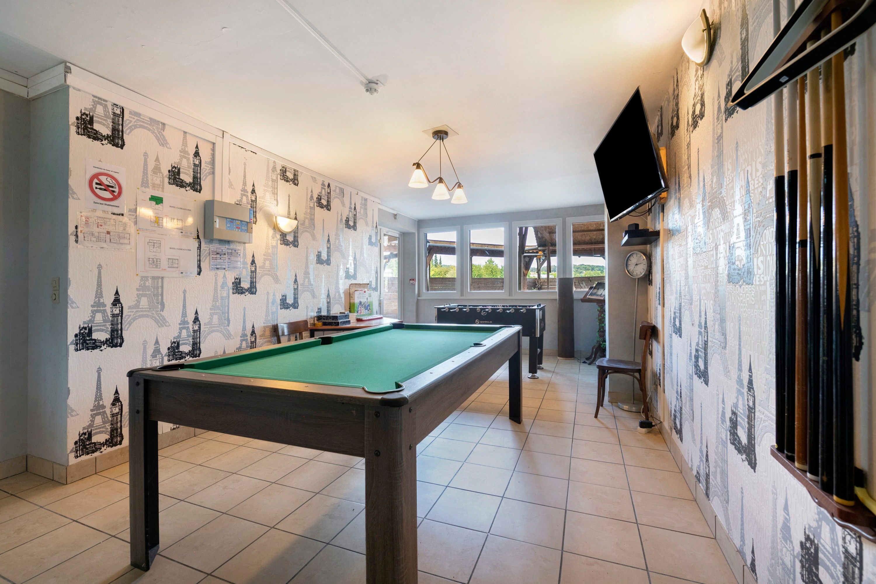 Een pooltafel in een ruimte met betegelde vloer, een bank en een aan de muur bevestigde televisie.