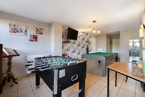 Een kamer met een tafelvoetbaltafel, een pooltafel en een aan de muur bevestigde televisie.