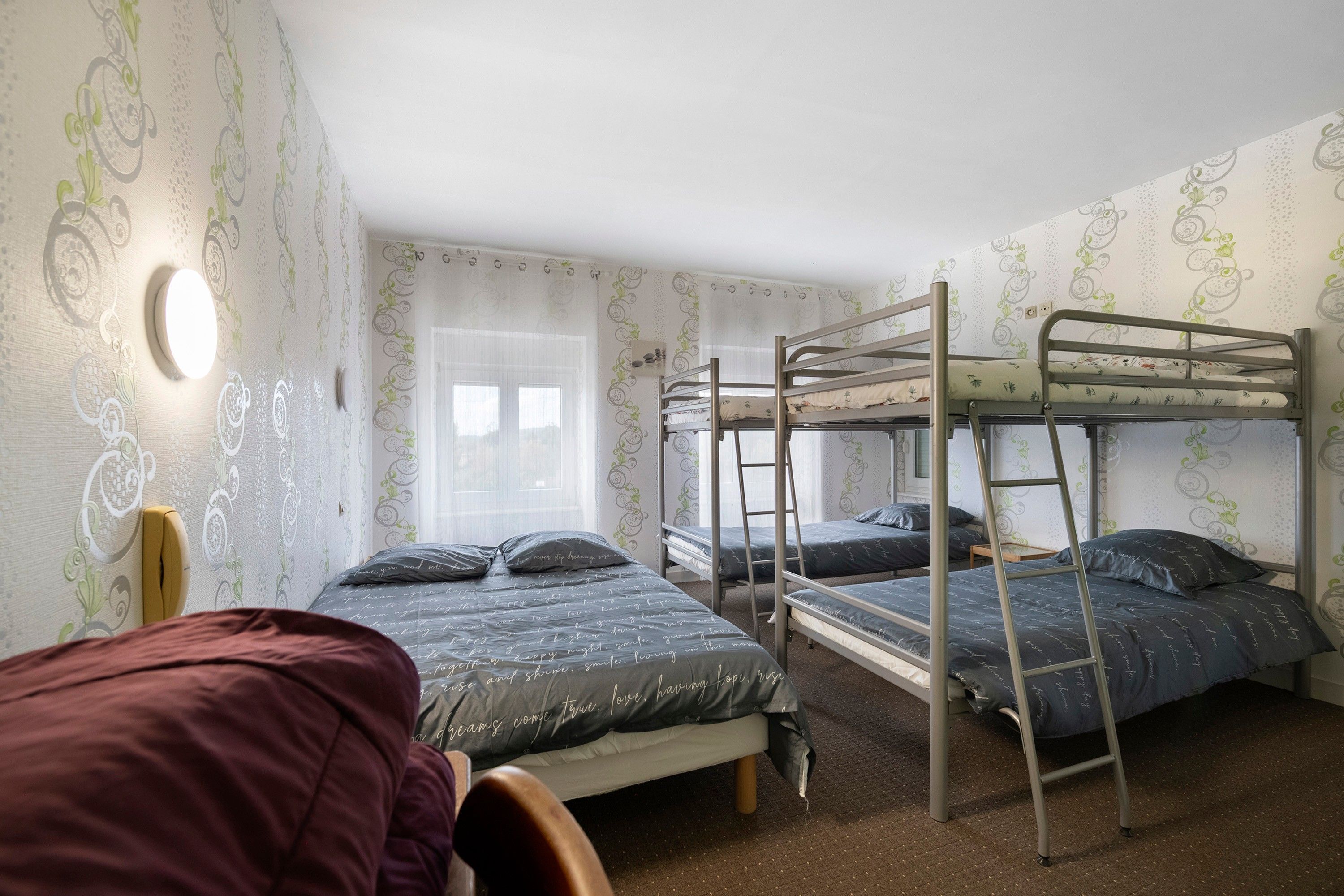 Een studentenkamer met stapelbedden, een raam met gordijnen en behang met een patroon.