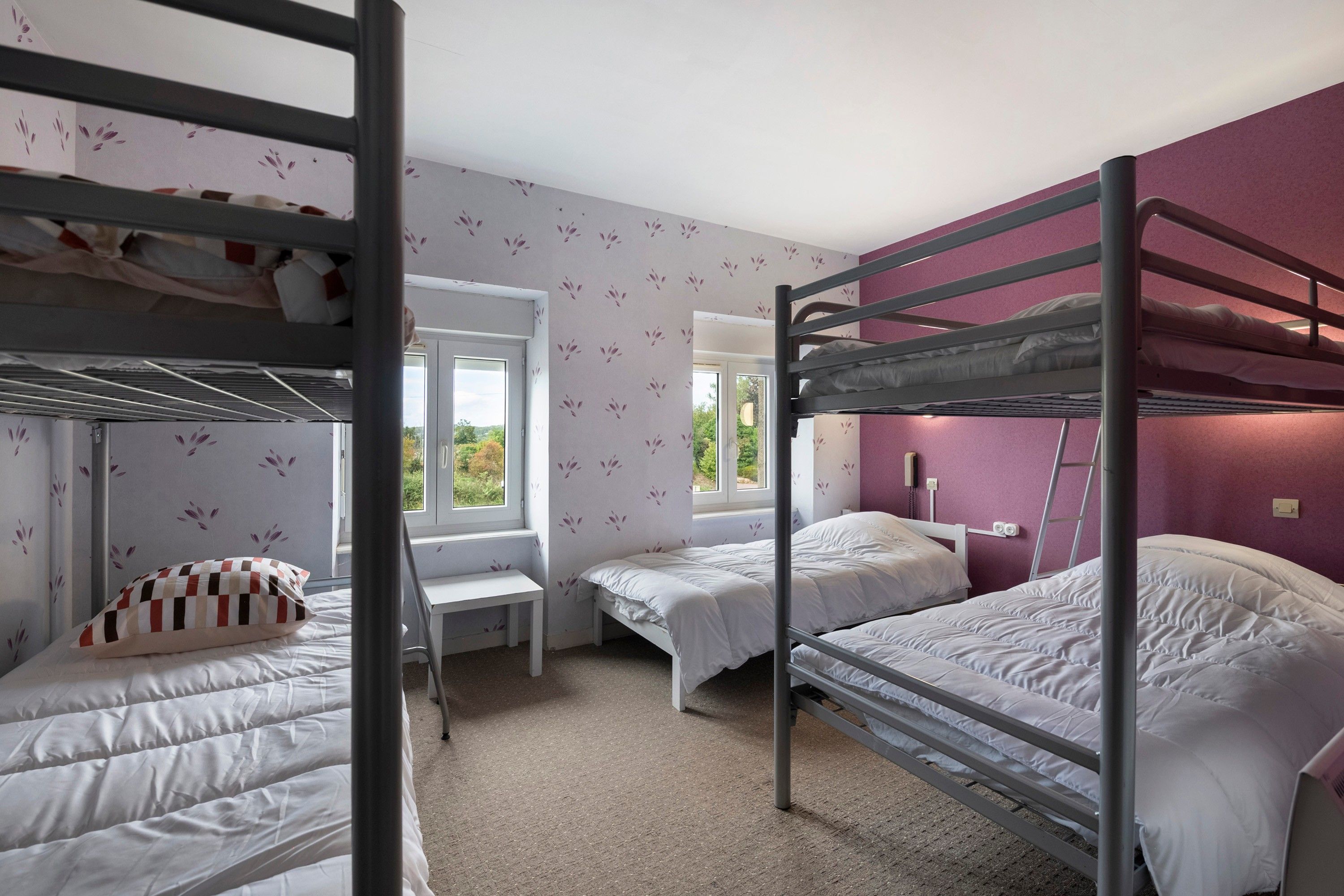 A dormitory room with bunk beds, a desk, and a window with a view of greenery.