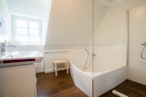 Ein modernes Badezimmer mit einer gläsernen Duschkabine, einem Holzschemel und einem weißen Waschbecken.