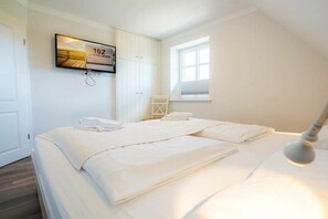 Een slaapkamer met twee bedden, een aan de muur bevestigde televisie en een raam dat natuurlijk licht biedt.