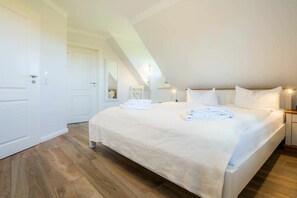 Ein Schlafzimmer mit einem großen Bett, weißen Wänden und einer geneigten Decke.