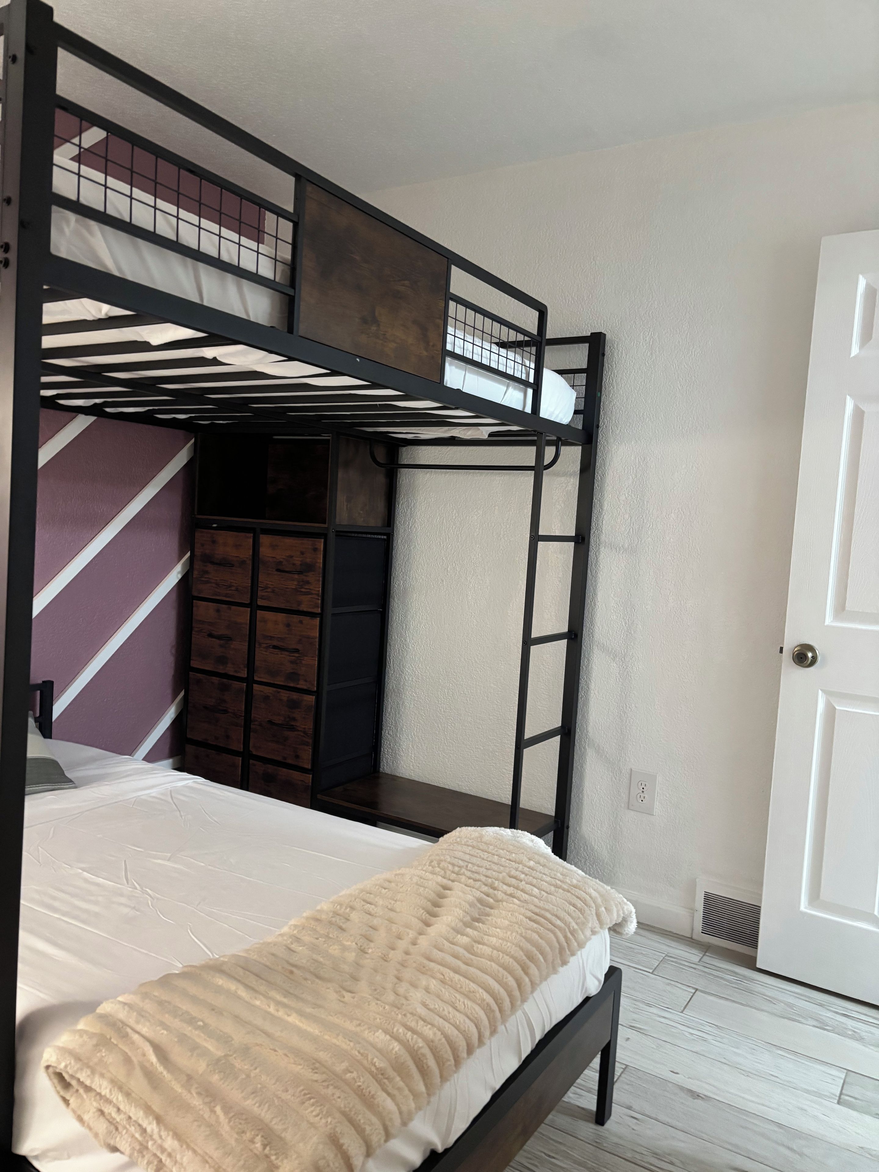 A bunk bed with a mattress and a blanket, a wooden wardrobe, and a white door.