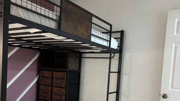 A bunk bed with a mattress and a blanket, a wooden wardrobe, and a white door.
