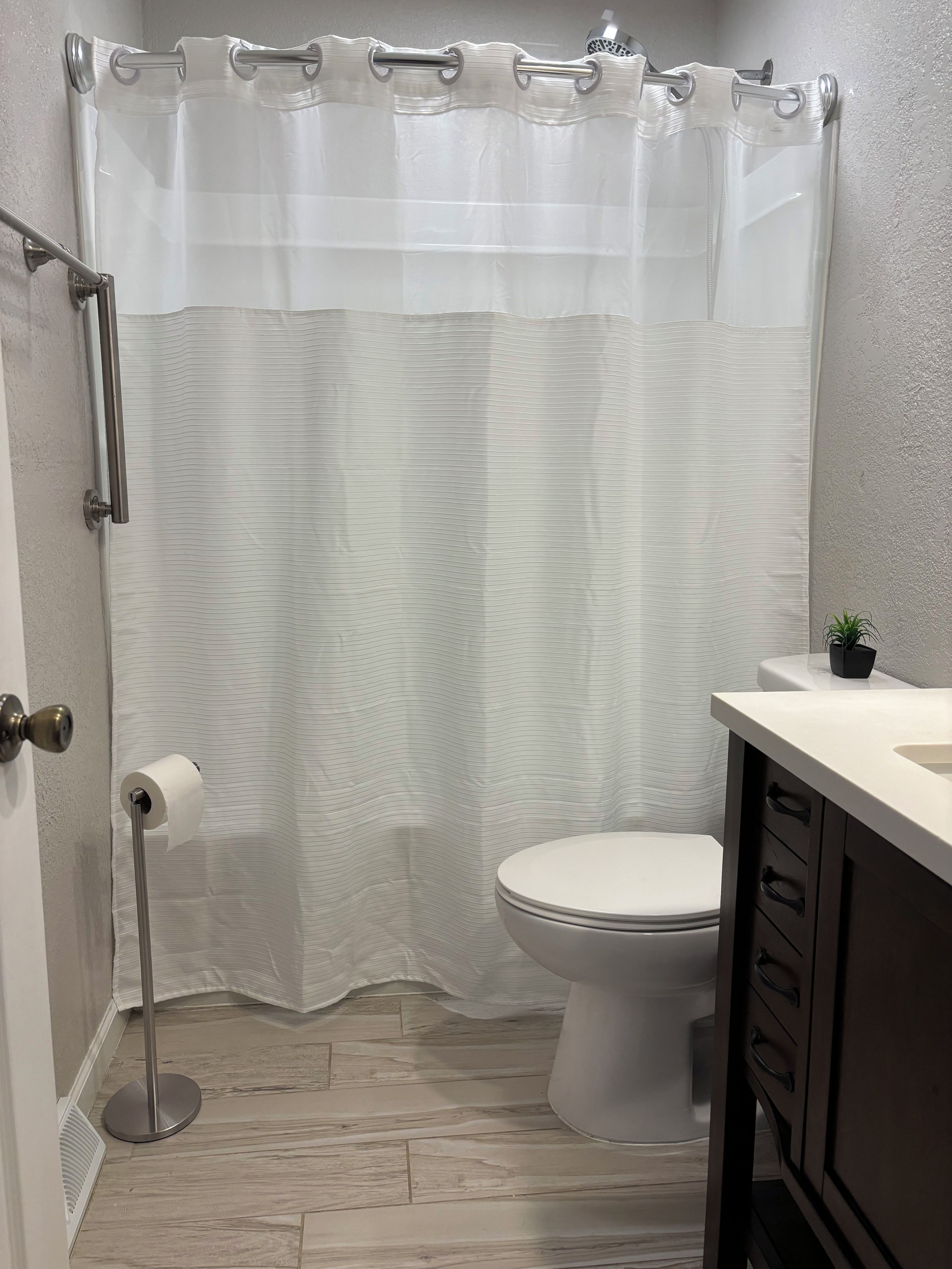 A bathroom with a toilet, a sink, a shower curtain, and a toilet paper holder.