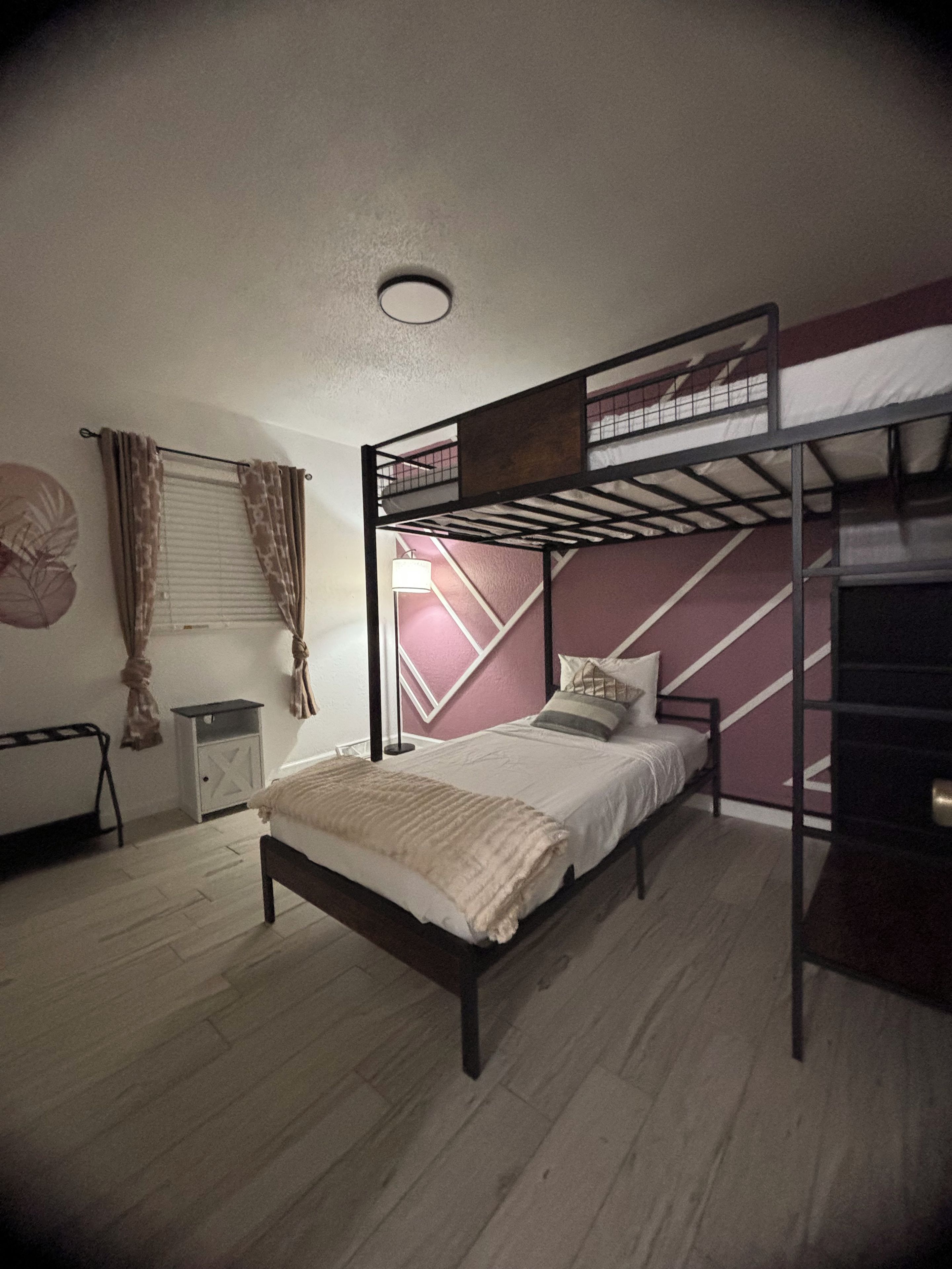Une chambre avec un lit superposé, un lit simple, une petite table, une lampe et un radiateur.