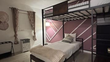Une chambre avec un lit superposé, un lit simple, une petite table, une lampe et un radiateur.