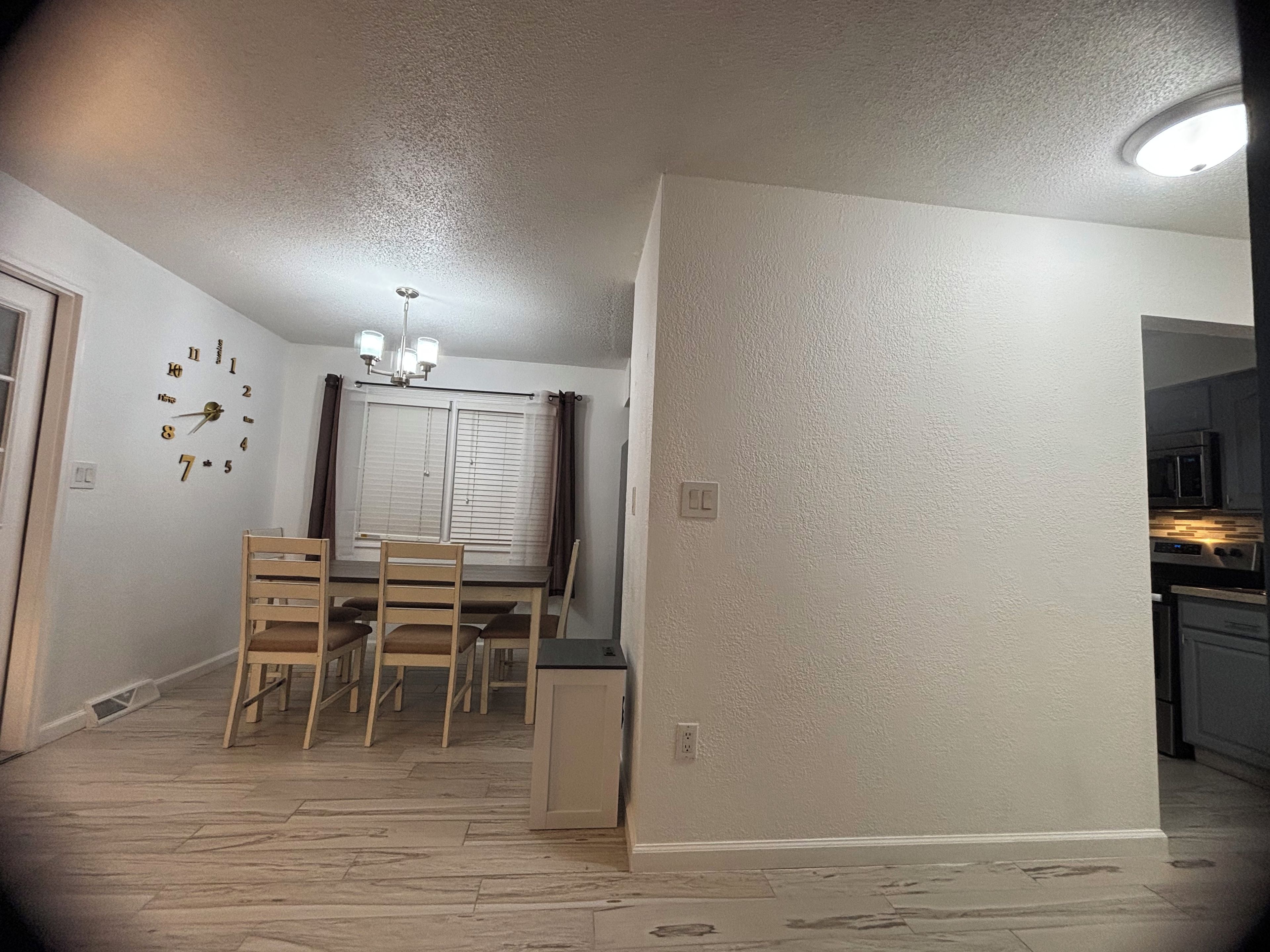 A dining area with a table and chairs, a wall clock, and a ceiling light fixture.