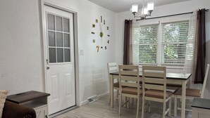 Un coin repas avec une table et des chaises, une porte blanche et une fenêtre avec des stores.