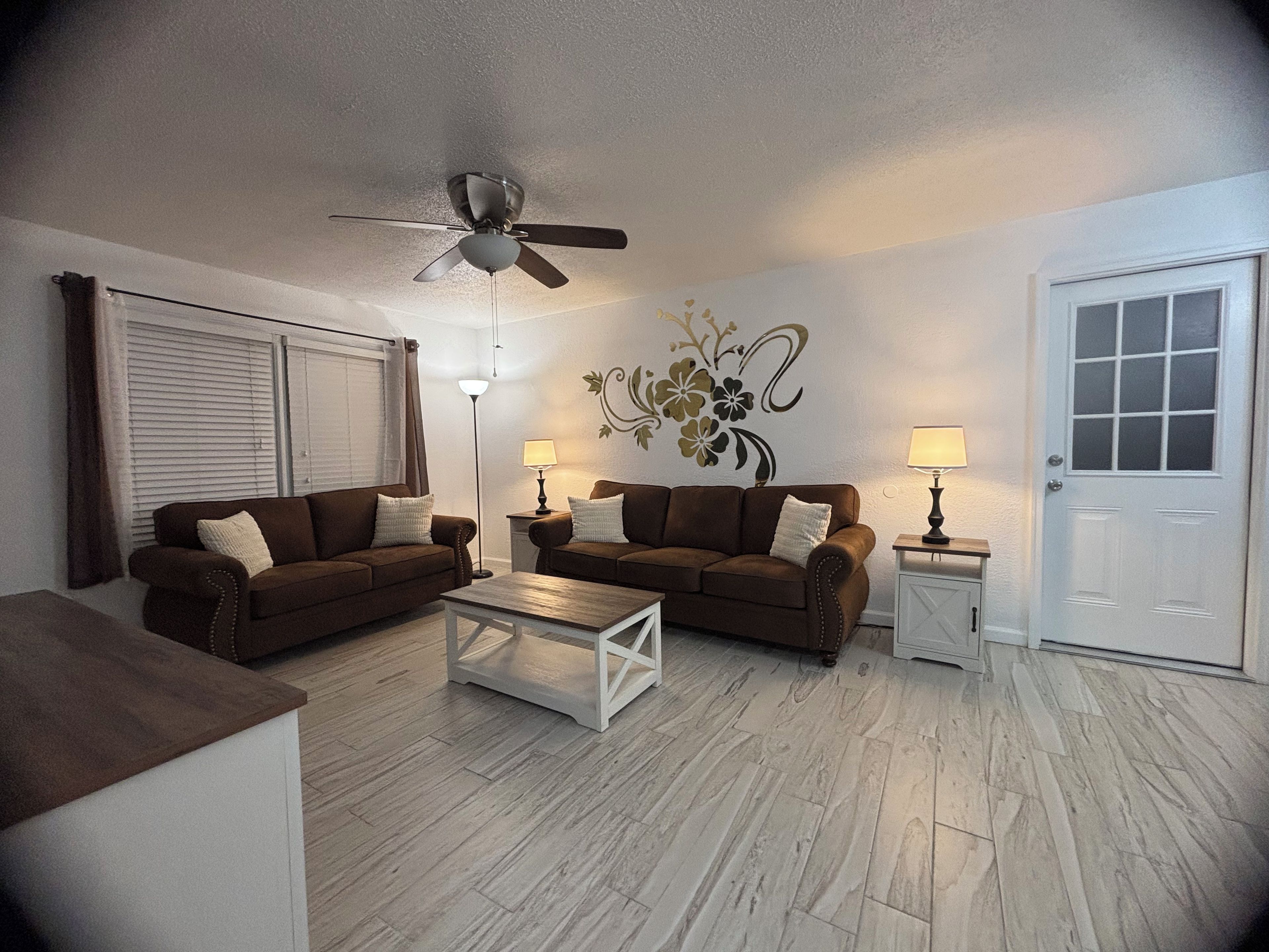 A living room with two sofas, a coffee table, a ceiling fan, and a door.