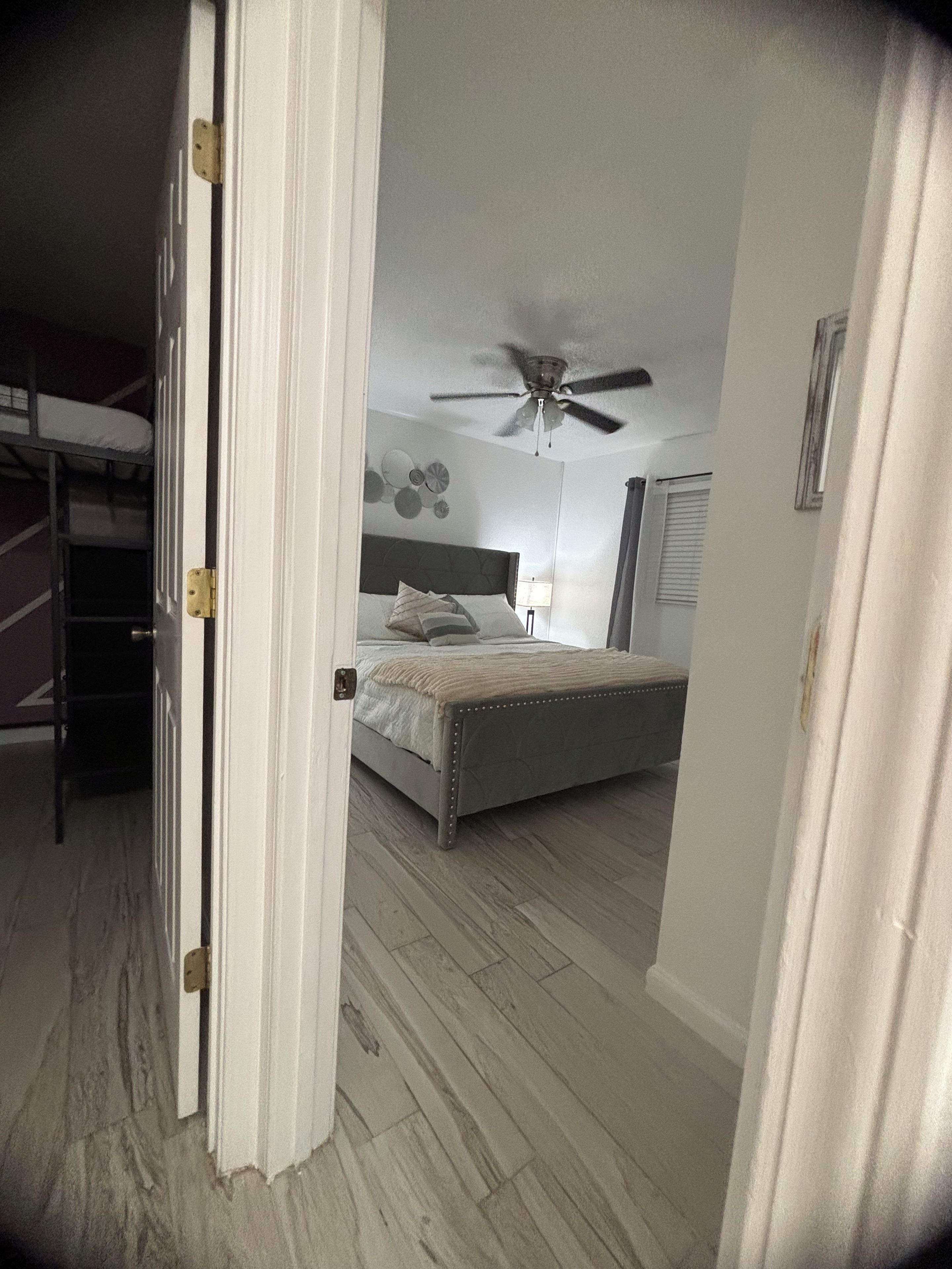 A bedroom with a bed, a ceiling fan, a bedside lamp, and a bunk bed in the adjacent room.