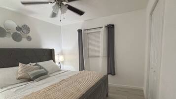 A bedroom with a bed, a ceiling fan, a window with curtains, and a wall-mounted light.