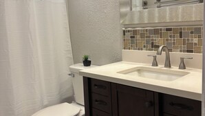 Une salle de bain équipée de toilettes, d’un lavabo, d’un miroir et d’un rideau de douche.