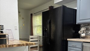 Une cuisine avec un réfrigérateur noir, une machine à café et une poubelle.