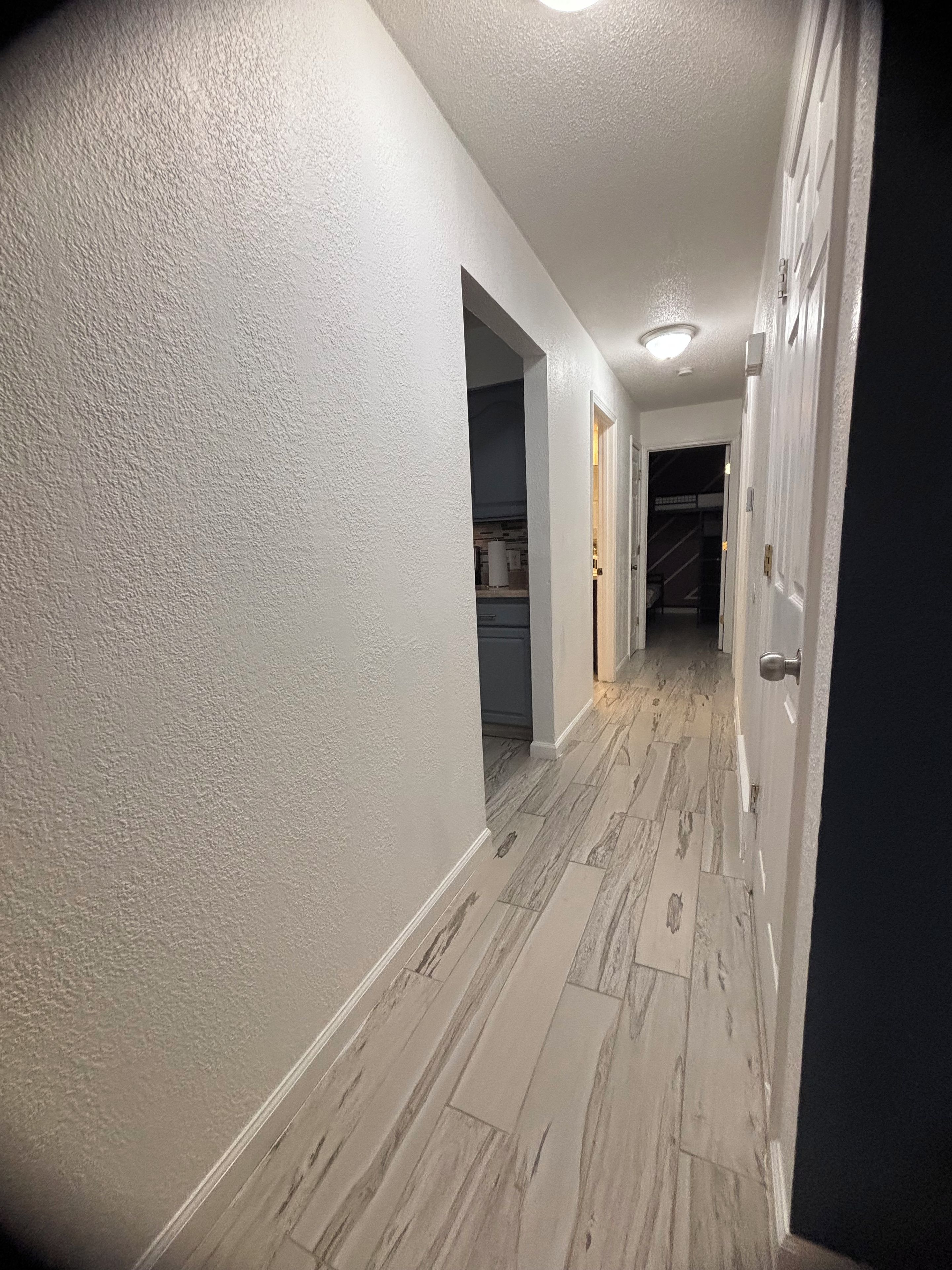 A hallway with white walls, a marble floor, and a door on the right.