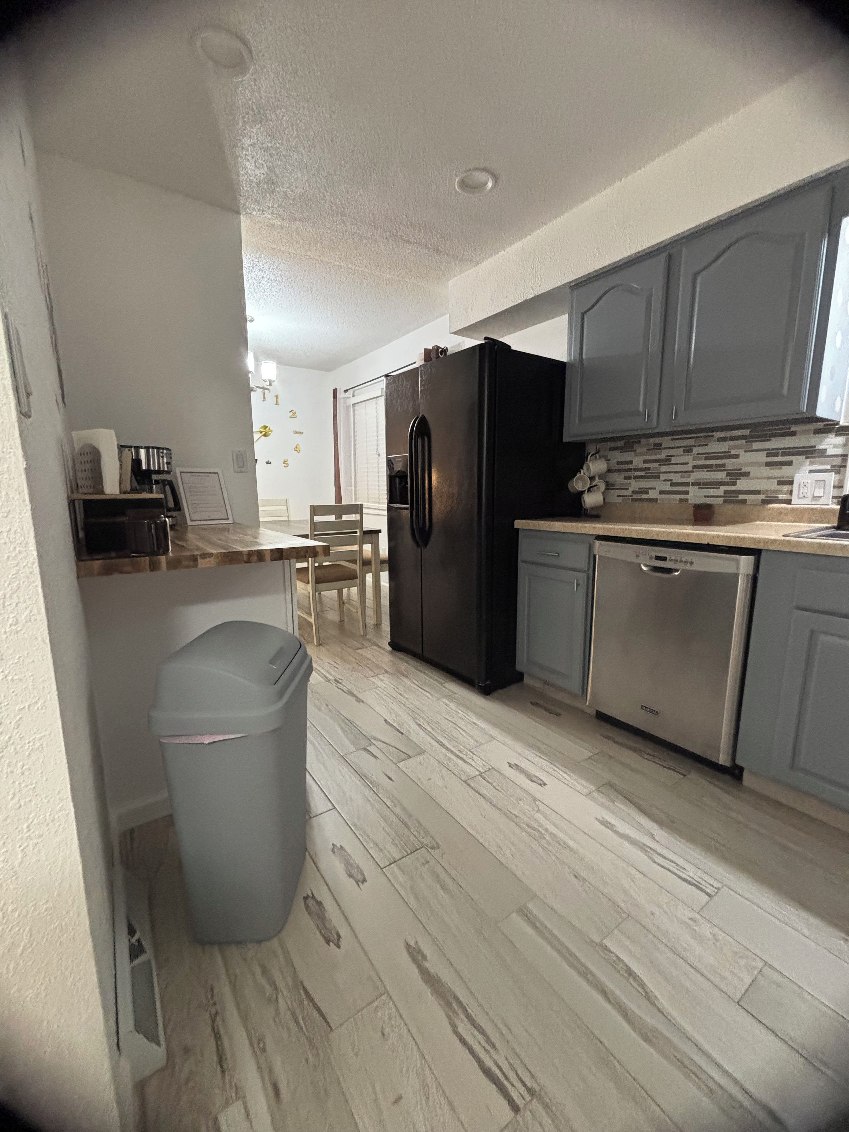 A compact kitchen with a refrigerator, dishwasher, and a trash bin.