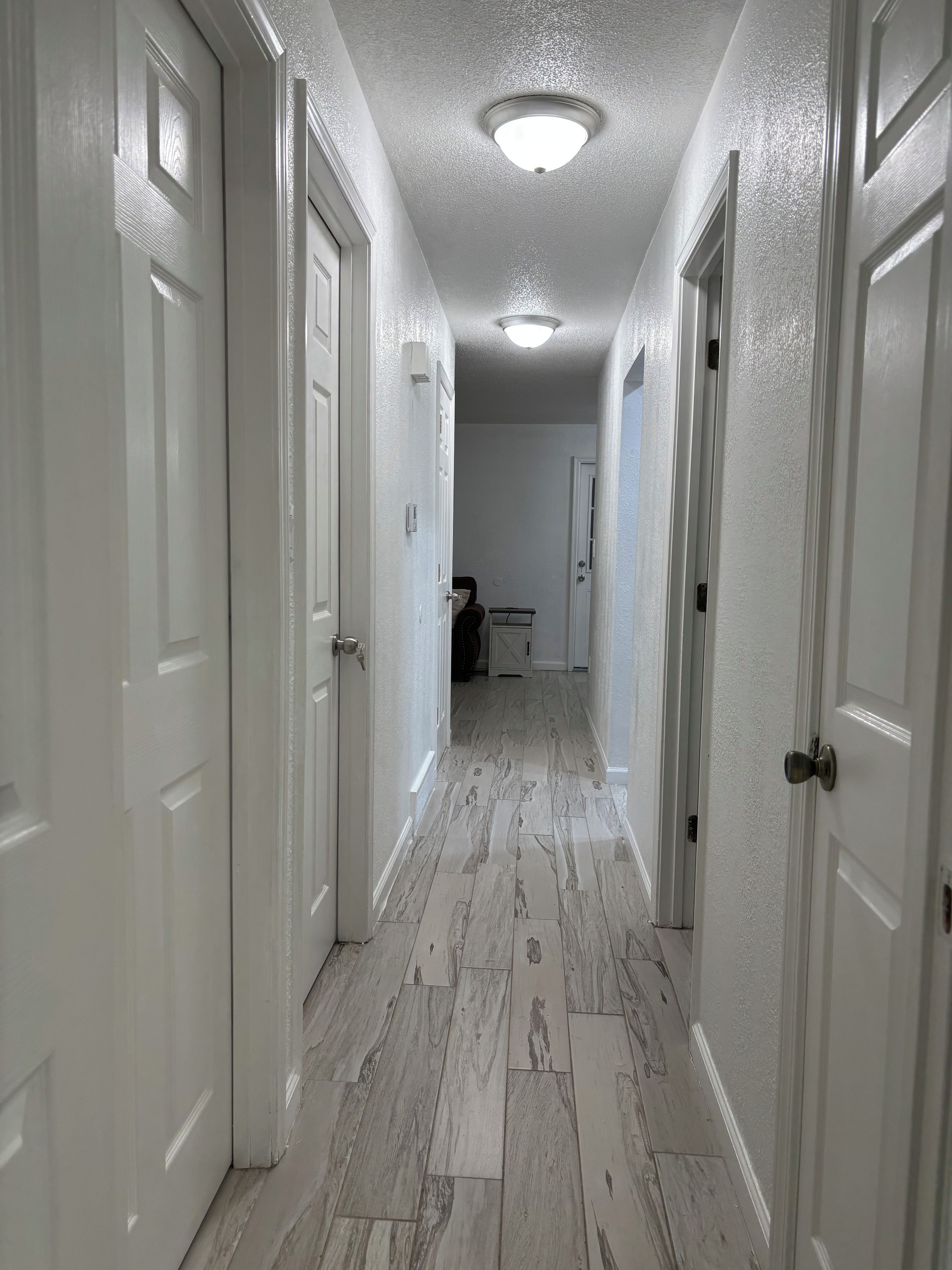 A hallway with white doors, a ceiling light, and a floor with a wood-like pattern.