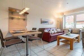 Ein Wohnzimmer mit Essbereich, einem roten Sofa, einem Holztisch und einem Fenster mit Vorhängen.