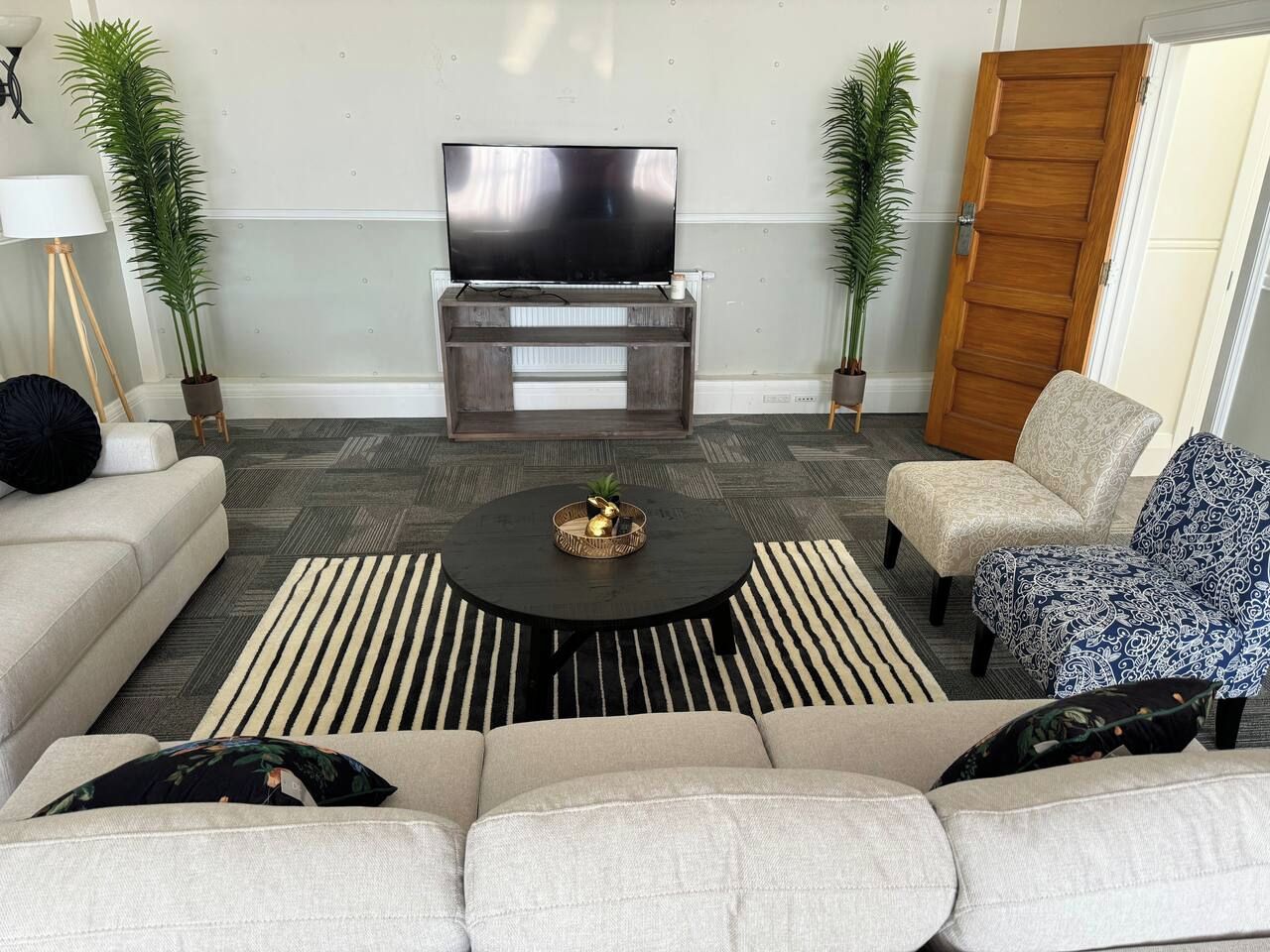 A living room with a sofa, armchairs, a coffee table, a TV on a stand, and two potted plants.