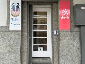A building entrance with a white door, a mailbox, and two signs: one for Taku Aroha and another for Airbnb.