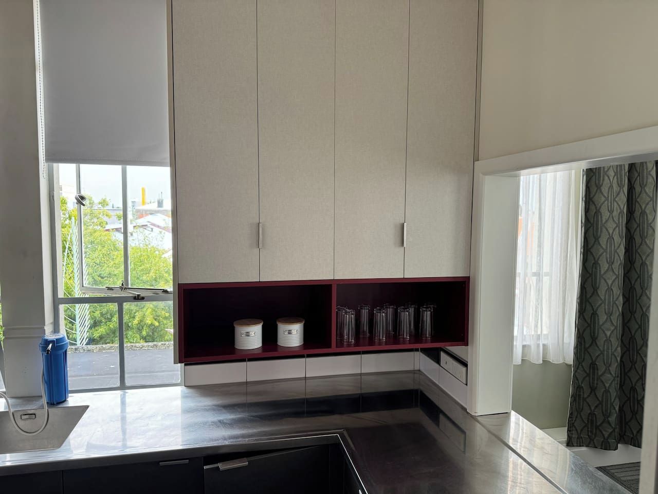 Una cocina moderna con horno empotrado, ventana con vistas y estante rojo con utensilios de cocina.