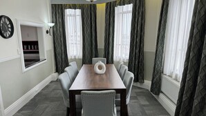 Een vergaderruimte met een houten tafel, zes stoelen, een klok en gordijnen met een patroon.