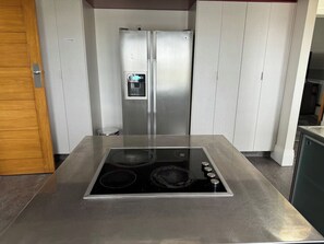 A kitchen with a stainless steel refrigerator, double doors, and a black induction cooktop with four burners.