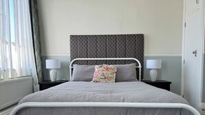 Een hotelkamer met een bed, twee nachtkastjes, een raam met gordijnen en een radiator.