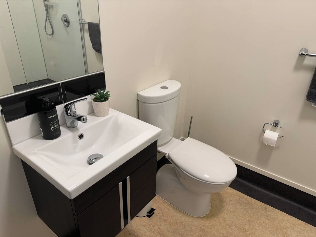 Un baño con lavamanos blanco, armarios negros, un inodoro, un espejo y una planta pequeña en maceta.
