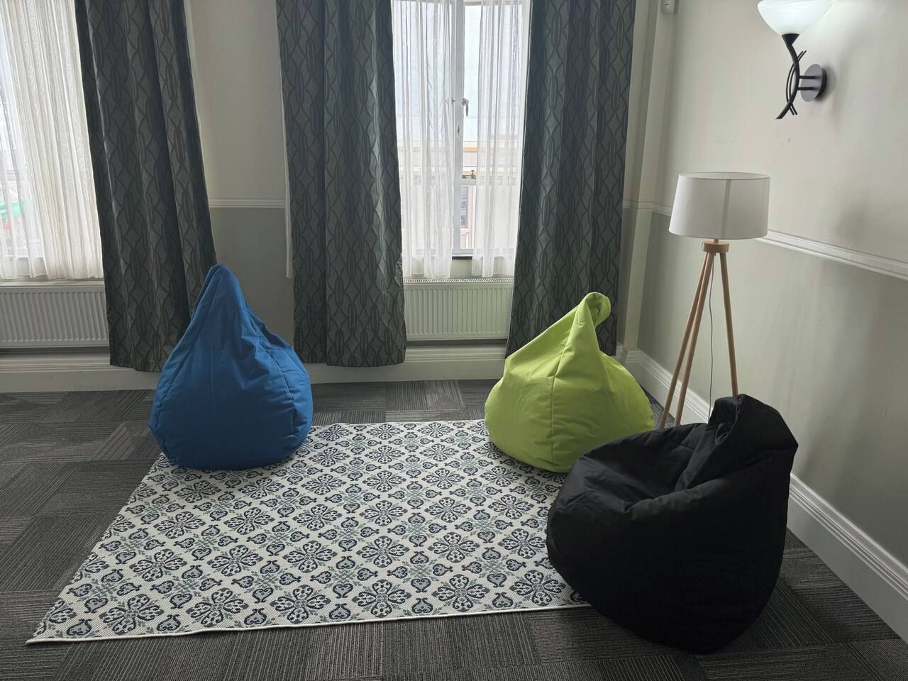 A room with a patterned rug, three bean bags, a lamp, and a window with curtains.