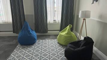 A room with a patterned rug, three bean bags, a lamp, and a window with curtains.
