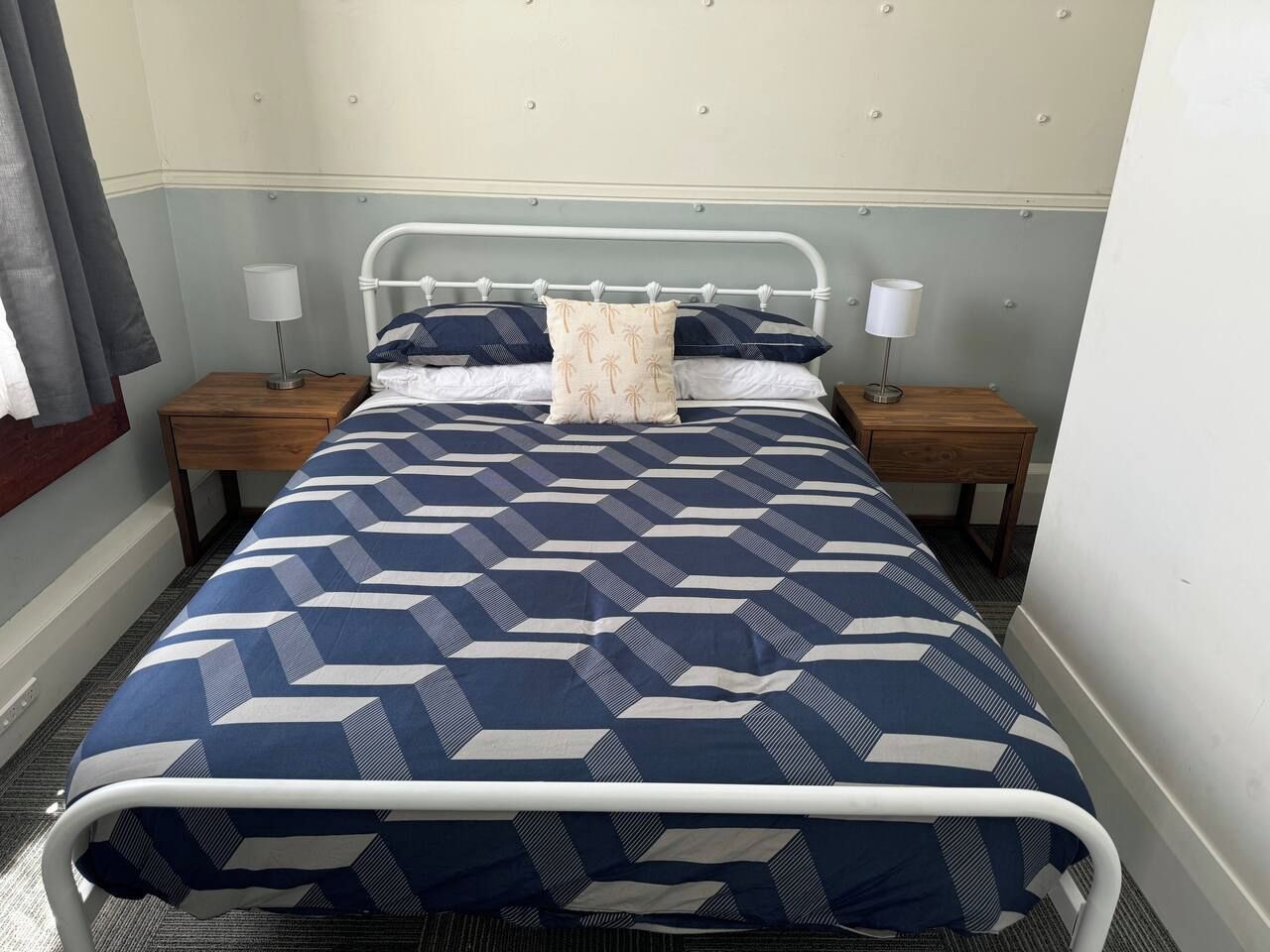 Un lit recouvert d’une couvre-lit à motifs géométriques, deux tables de chevet avec des lampes et une tête de lit à motifs capitonnés.