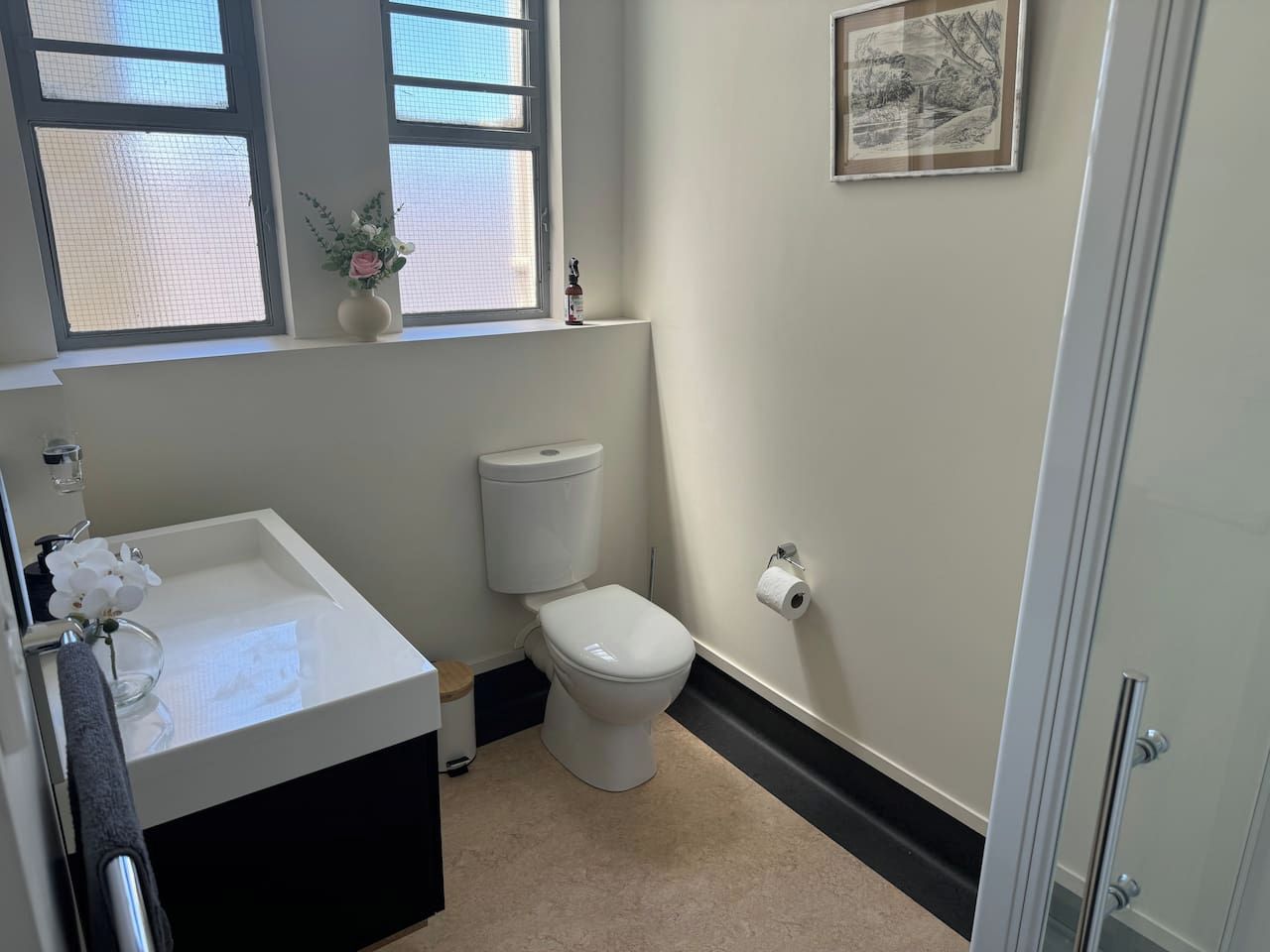 A bathroom with a white sink, toilet, and a window with a view of the outdoors.