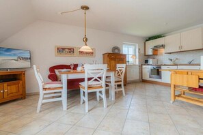 A dining area with a table and chairs, a kitchen with cabinets and appliances, and a television on a cabinet. - Holiday apartment 4 "Müller" (ID 425) (St. Peter-Böhl)