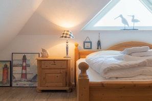 A bedroom with a bed, a nightstand, a lamp, a window with a view of birds, and two framed pictures on the wall. - Holiday apartment 4 "Müller" (ID 425) (St. Peter-Böhl)