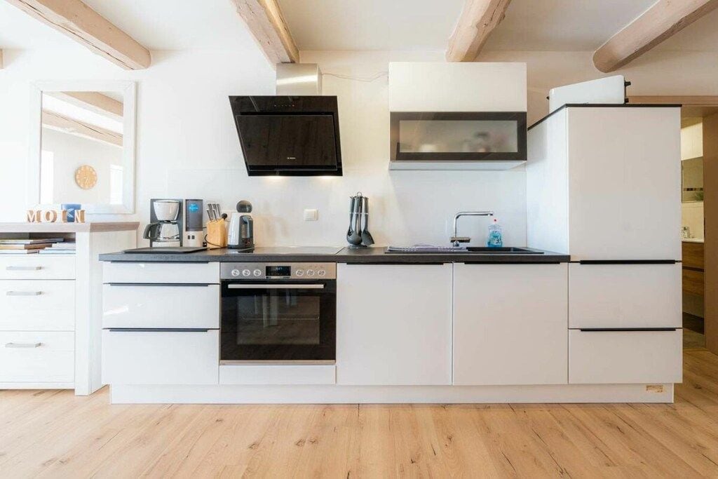 Eine moderne Küche mit weißen Schränken, einem eingebauten Backofen, einer Mikrowelle und einer Kaffeemaschine.
