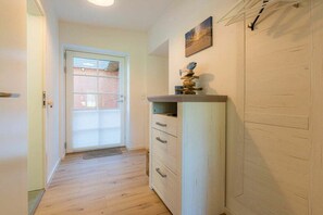Ein Flur mit Holzboden, einer Tür, die nach draußen führt, und einem weißen Schrank mit Schubladen.