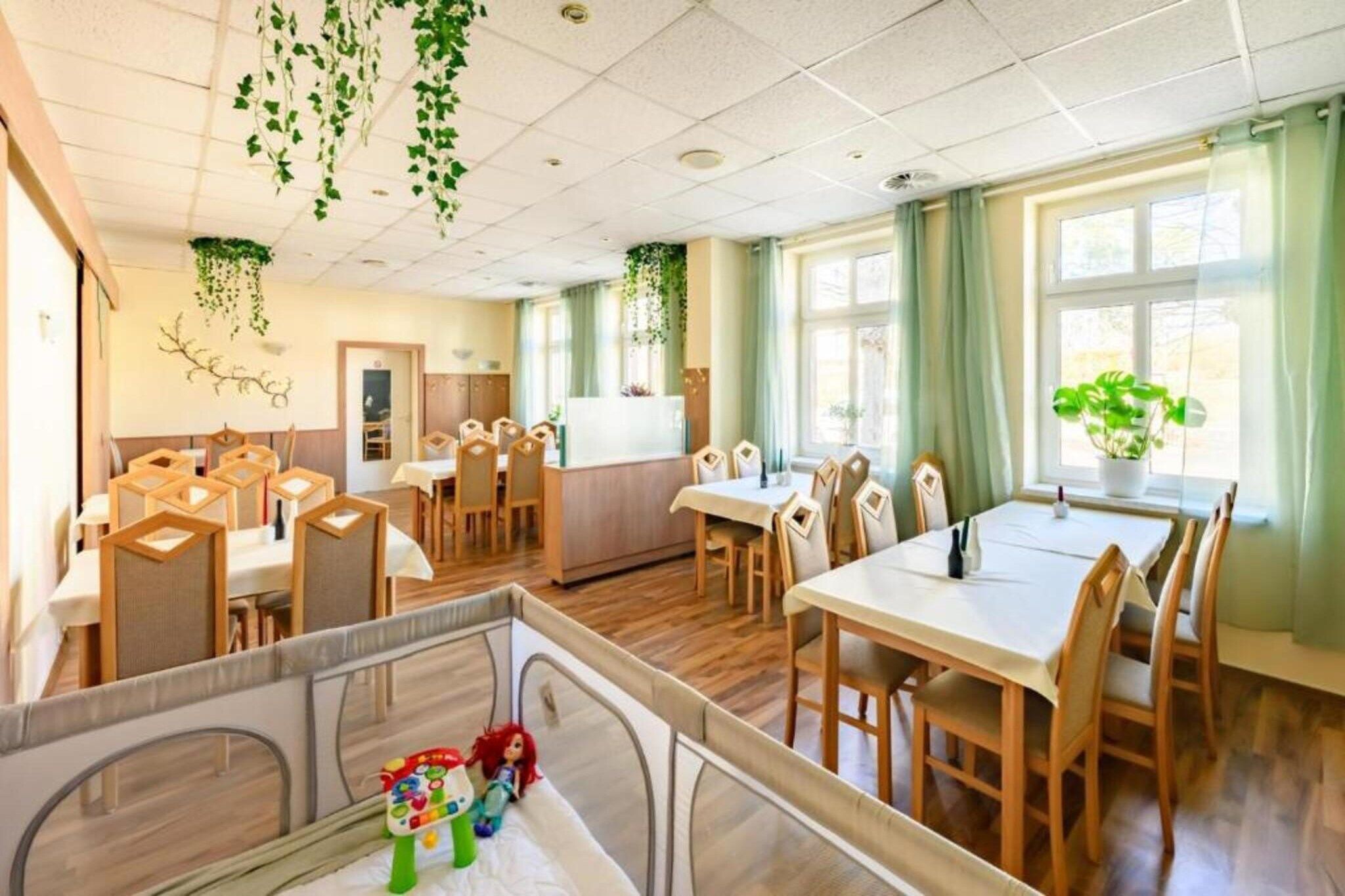 A dining area with wooden chairs and tables, a children's play area with toys, and hanging plants.