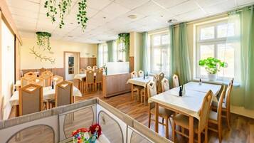 A dining area with wooden chairs and tables, a children's play area with toys, and hanging plants.