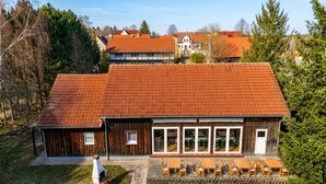 A two-story building with a red-tiled roof, a wooden exterior, and a patio with outdoor seating. - Landhotel lindengarten by Belvilla- Standard Double Room (Rheinsberg)
