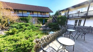A courtyard with a small pond, outdoor seating, and a building with a balcony. - Landhotel lindengarten by Belvilla- Standard Double Room (Rheinsberg)