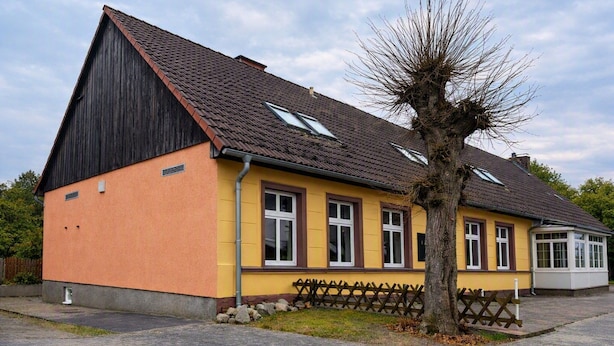 A two-story building with a sloped roof, dormer windows, and a tree in front. - Landhotel lindengarten by Belvilla- Standard Double Room (Rheinsberg)