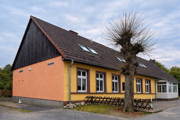 Ein zweistöckiges Gebäude mit Satteldach, Dachgauben und einem Baum davor.