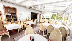 A restaurant with round tables and wicker chairs, a bar area, and a view through large windows. - Landhotel lindengarten by Belvilla- Standard Double Room (Rheinsberg)
