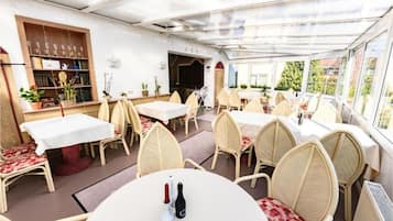 A restaurant with round tables and wicker chairs, a bar area, and a view through large windows.